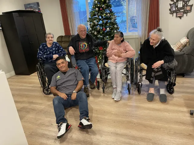 Residents and a caregiver together in the living room beside the Christmas tree.
